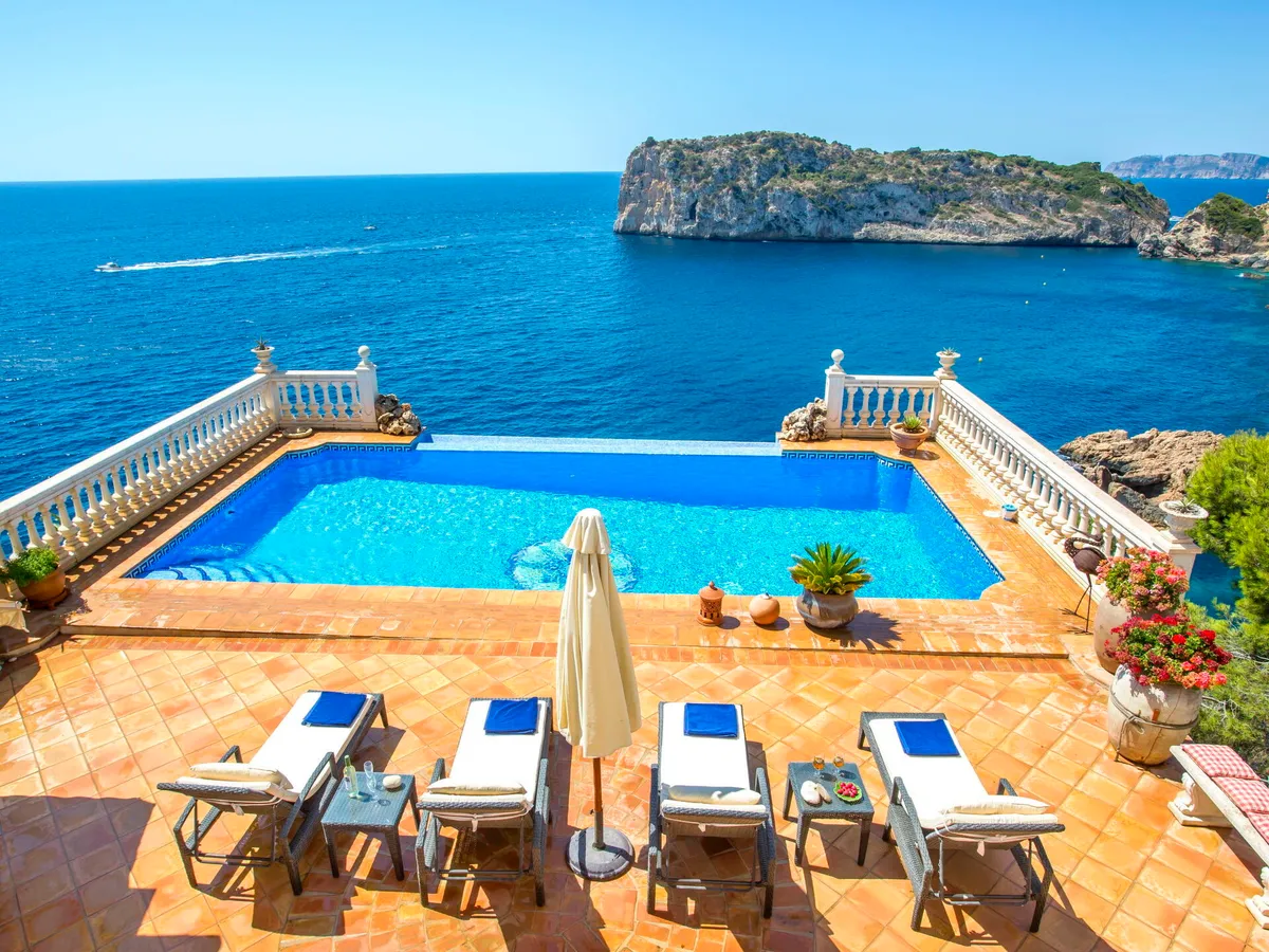 Villa Lauras Paradise's infinity pool and terracotta terrace with sun loungers offer stunning views of the Mediterranean Sea and a rocky island in Jávea, Valencia.