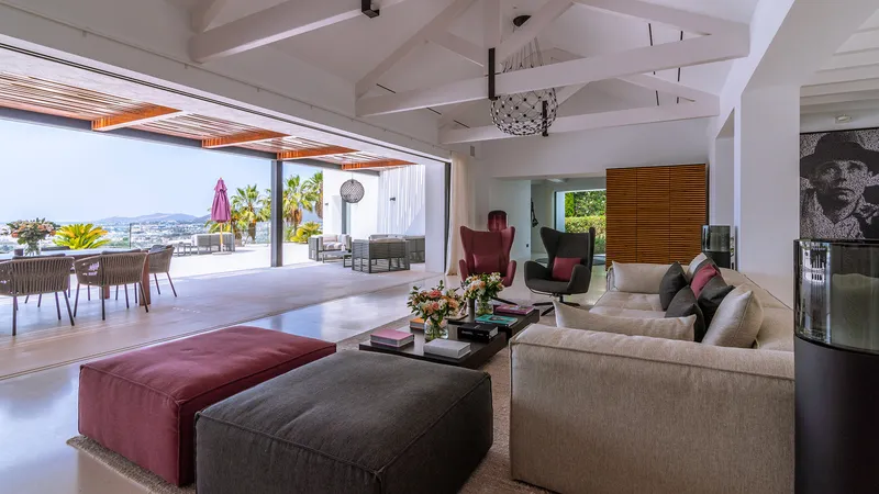 Villa Amanecer — Open living room and terrace Villa Amanecer's expansive living room opens to a luxurious terrace with dining and lounge areas, offering stunning views of Ibiza.