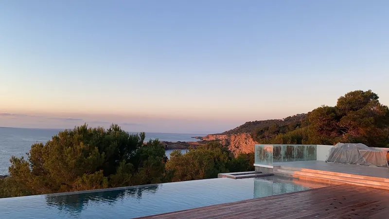 Villa Fred's infinity pool overlooks the Mediterranean Sea and a lush coastline at sunset in Ibiza.