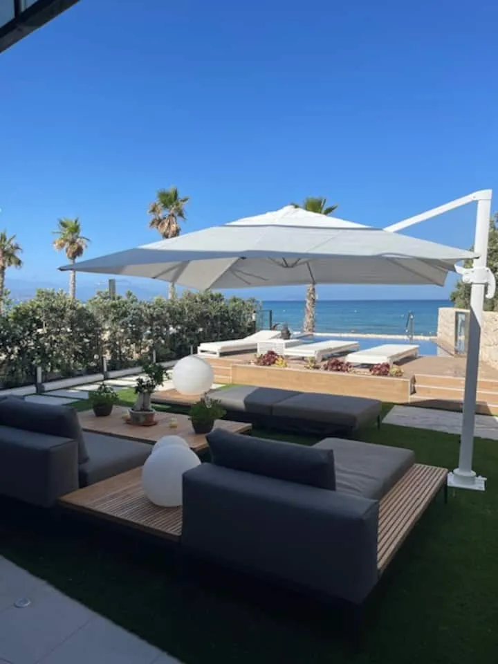 VILLA SEAS THE DAY — Outdoor lounge with ocean view VILLA SEAS THE DAY outdoor lounge area featuring modern seating, a large umbrella, infinity pool, and ocean views in Alicante, Spain.