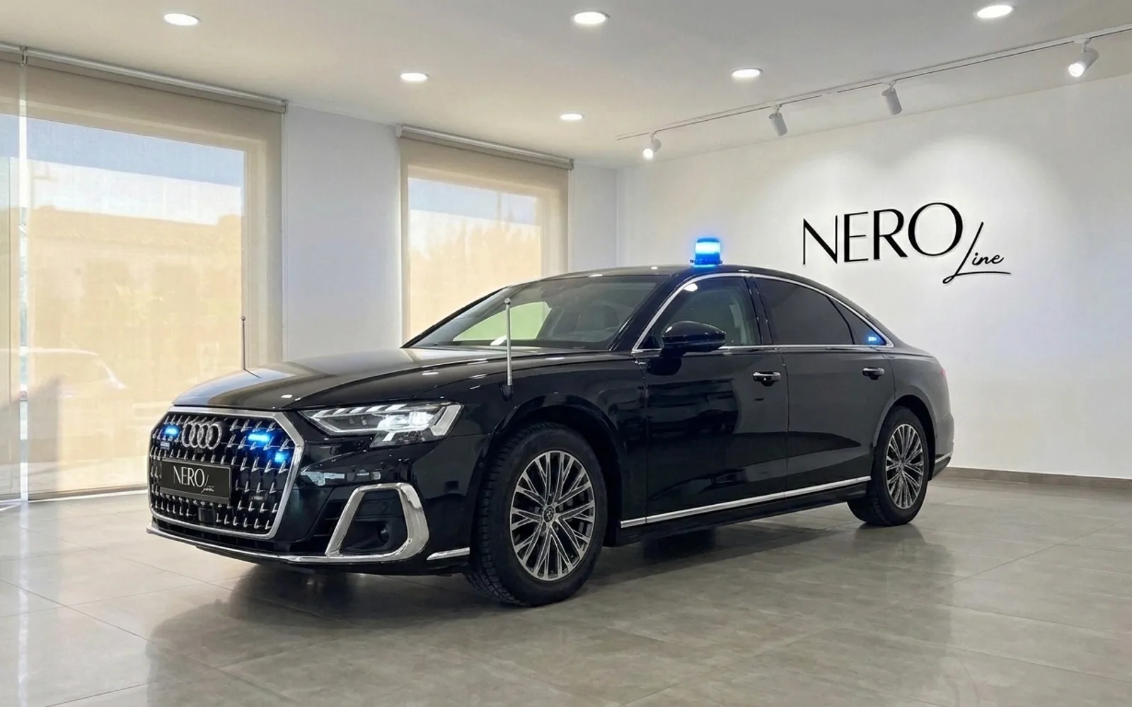 The black Audi A8 L VR10 Armoured car is parked in a modern showroom in Madrid, featuring a blue emergency light on its roof.