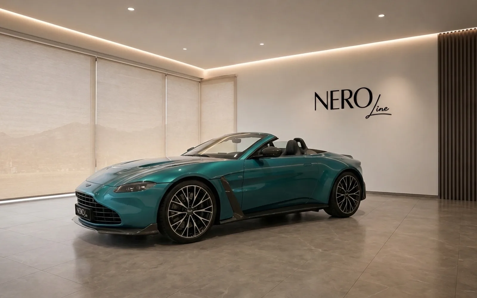 The metallic teal Aston Martin Vantage V8 Roadster is showcased in a modern showroom with its convertible top down.
