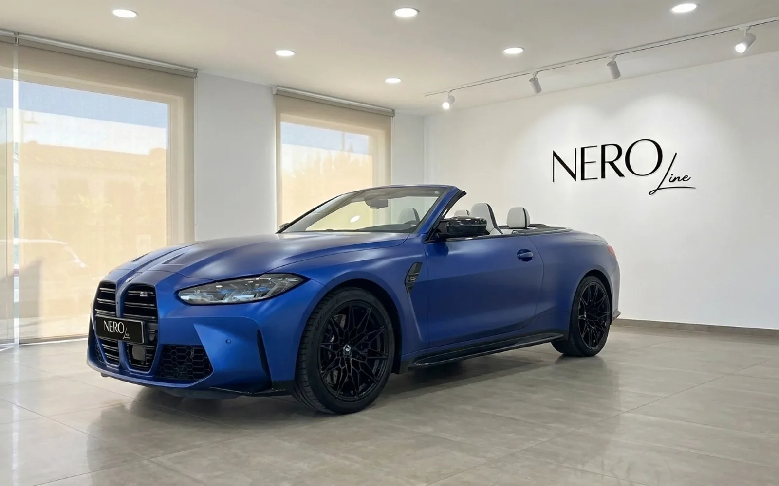 El BMW M4 Competition Cabrio 2023 en azul Frozen Portimao mate, descapotado, se exhibe en un luminoso showroom de Ibiza.