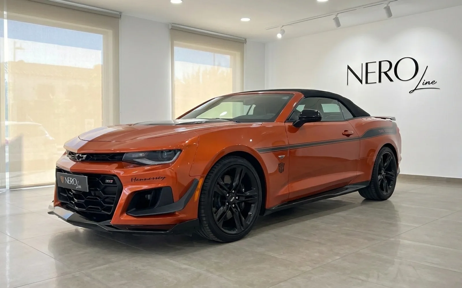 Un Chevrolet Camaro Cabriolet naranja metálico brillante, un deportivo descapotable, se exhibe en un concesionario en Alicante, España, desde una vista frontal tres cuartos.