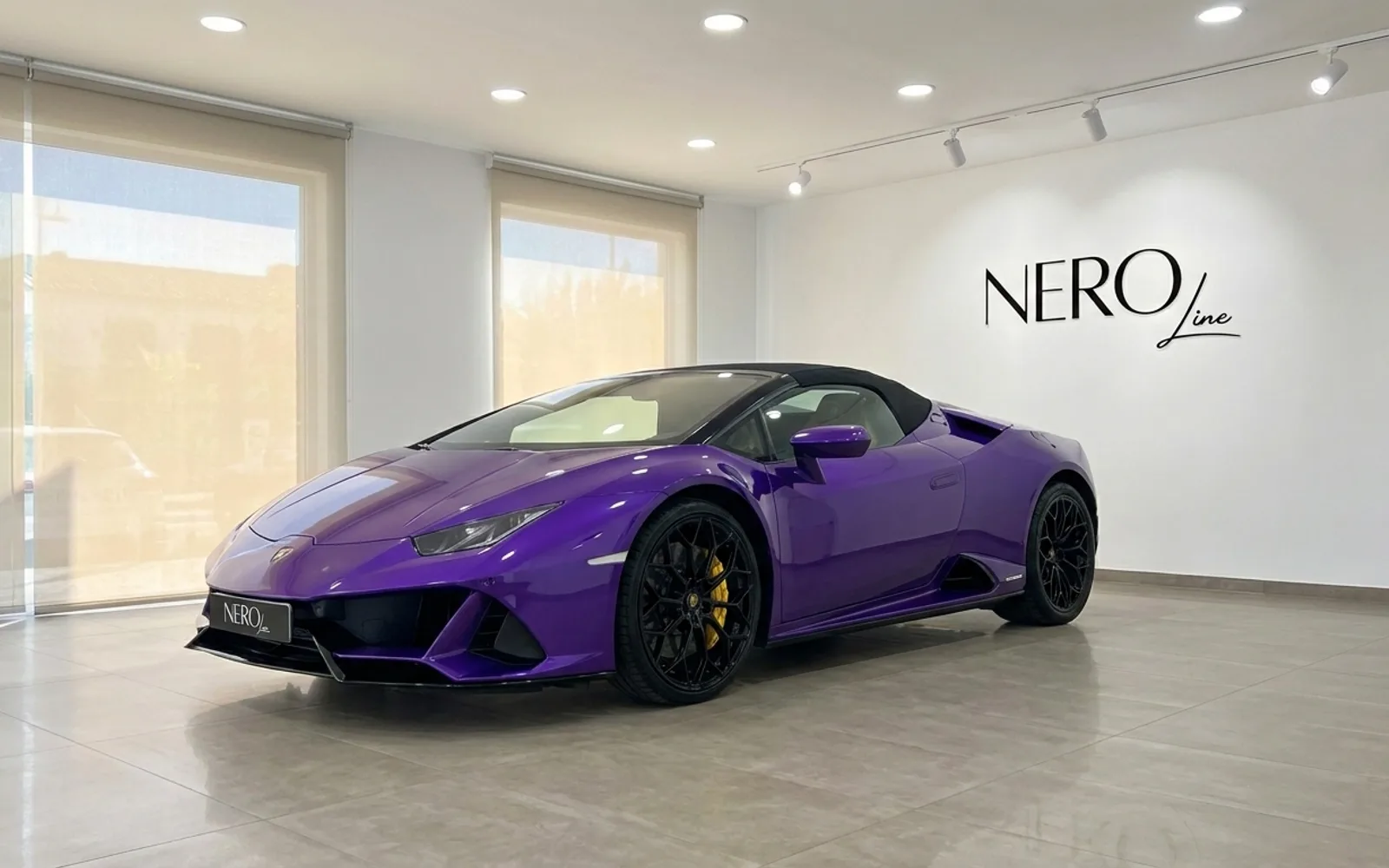 Lamborghini Huracán EVO Spyder — Luxury Rental Ibiza A vibrant purple Lamborghini Huracán EVO Spyder convertible is parked in a bright showroom with the Nero Line logo on the wall in Ibiza.