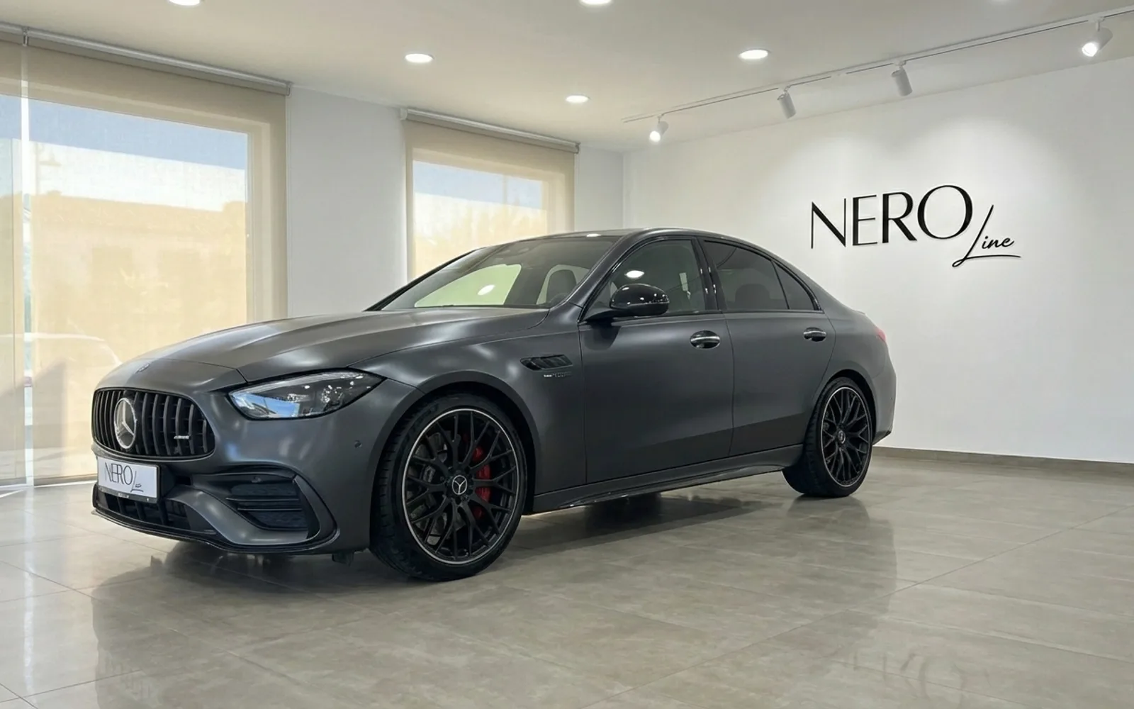 Mercedes-Benz C63 AMG — Luxury sedan in Alicante The dark metallic grey 2024 Mercedes-Benz C63 AMG luxury sedan is showcased from a front three-quarter angle in a bright Alicante showroom.