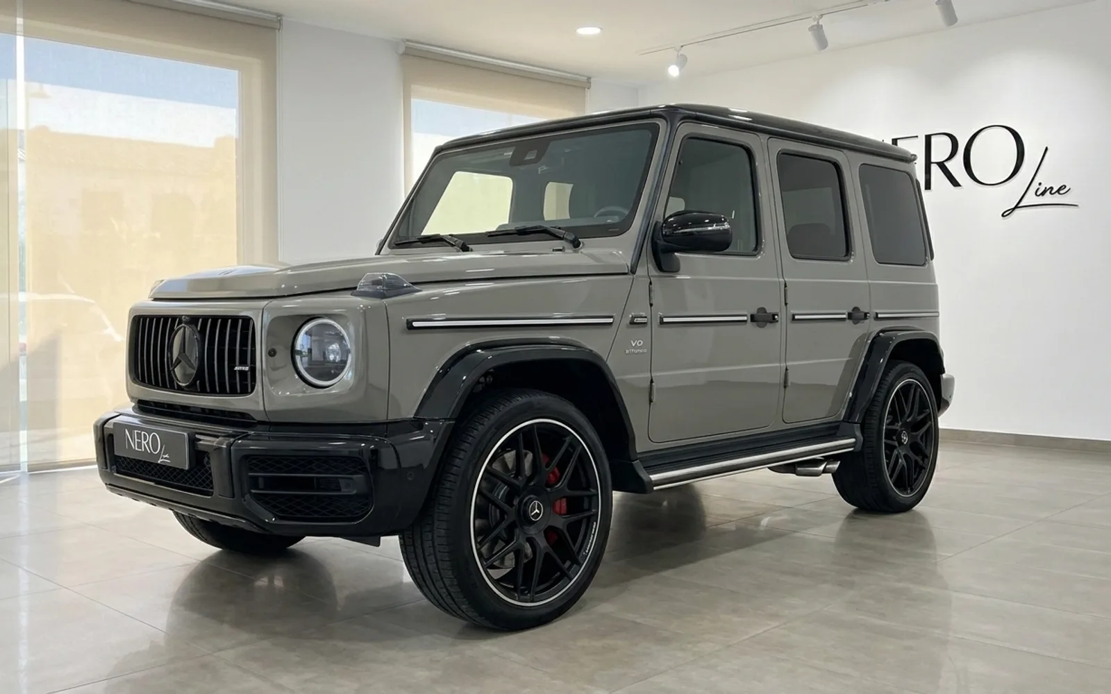 The gloss Arabian Grey Mercedes-Benz G63 AMG is seen from a front three-quarter angle, parked indoors in Ibiza.