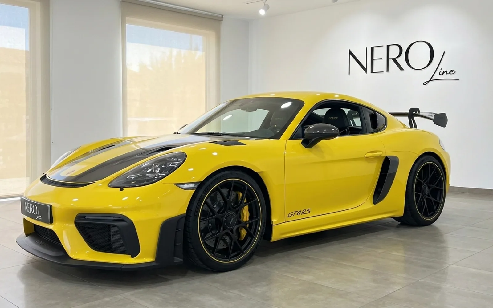 تُعرض سيارة بورش 718 كايمان GT4 RS الصفراء الزاهية من زاوية أمامية ثلاثية الأرباع في صالة عرض حديثة في أليكانتي.