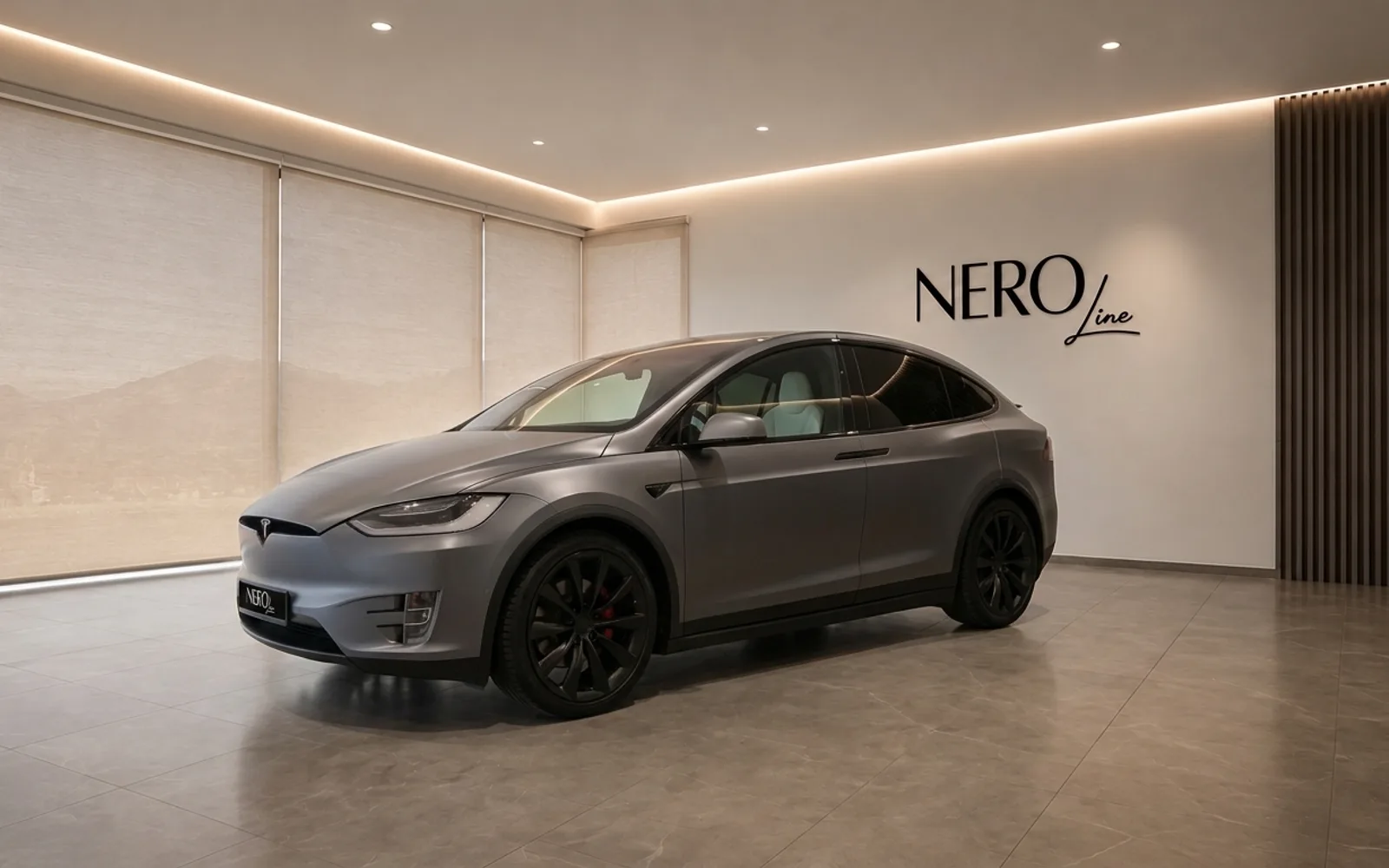 The 2021 Tesla Model X in satin Stealth Grey, shown from a front three-quarter view, parked in a modern showroom in Lausanne.