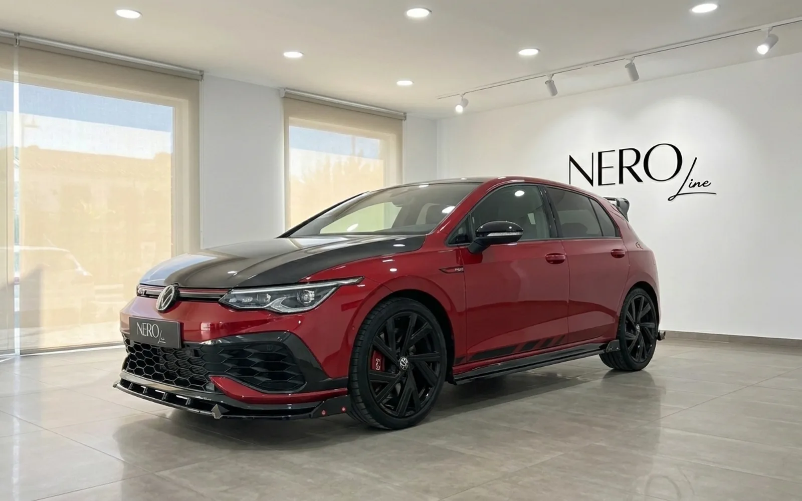 Volkswagen Golf GTI Clubsport — Concesionario Alicante El Volkswagen Golf GTI Clubsport en rojo Kings Red metálico brillante se exhibe desde un ángulo frontal tres cuartos en un moderno concesionario en Alicante.