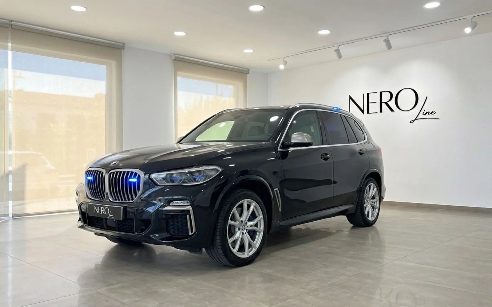 マドリードのショールームに駐車された、グリルとルーフに青い緊急灯を備えた黒いBMW X5 M装甲SUV。