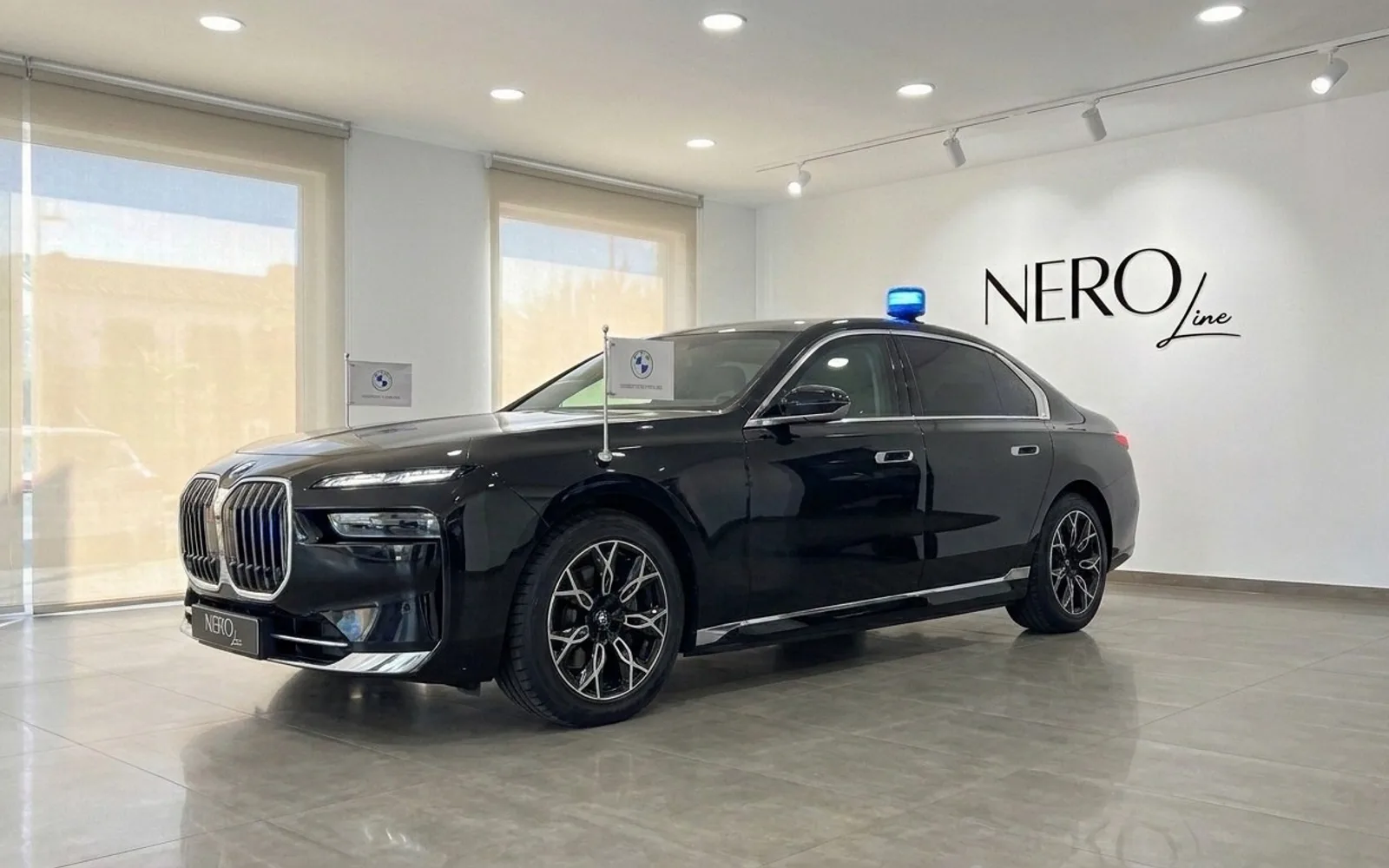 黒いBMW 7 Protectionがマドリードのショールームに展示されており、青いルーフライトとボンネットに旗が付いています。