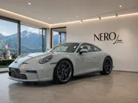 The Porsche GT3 RS in gloss Arctic Grey is showcased indoors, with a panoramic view of the Zurich mountains.