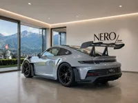 The gloss Arctic Grey Porsche GT3 RS is displayed in a modern showroom, with a stunning mountain landscape of Zurich visible through large windows.