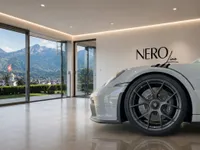 A gloss Arctic Grey Porsche GT3 RS front quarter view inside a modern showroom with panoramic mountain views in Zurich.