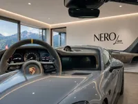The gloss Arctic Grey Porsche GT3 RS is displayed in a Zurich showroom, showcasing its front exterior and detailed interior with a mountain view.