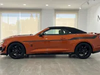 El Chevrolet Camaro Cabriolet 6.2 naranja, con capota negra y franjas de carreras, está aparcado en un moderno concesionario en Alicante.