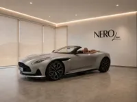 The metallic silver Aston Martin DB12 Volante, with its elegant brown leather interior, is showcased indoors in Lausanne.