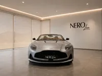 The Aston Martin DB12 Volante in metallic silver is prominently displayed from the front in a modern showroom in Lausanne.
