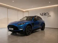 The blue Aston Martin DBX707 is parked in a modern showroom in Lausanne, showcasing its elegant front three-quarter view.