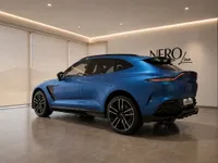 The gloss Ion Blue Aston Martin DBX707 is showcased from the rear three-quarter angle in a modern showroom in Lausanne.