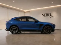 The blue 2023 Aston Martin DBX707, a performance SUV, is shown in a side profile view inside a modern showroom in Lausanne.