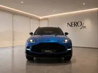 The gloss Ion Blue Aston Martin DBX707 is showcased from a direct front view in a modern showroom in Lausanne.