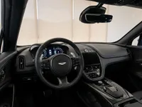 The luxurious cockpit of the Aston Martin DBX707 in Lausanne, featuring a multi-function steering wheel, digital dashboard, and blue stitching.