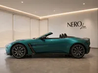 The Metallic Teal Aston Martin Vantage V8 Roadster is shown in side profile with its top down, parked in a Lausanne showroom.