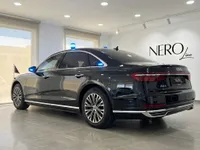 The black Audi A8 L VR10 Armoured car, with blue emergency lights and a flag, is shown from a rear three-quarter angle inside a Madrid showroom.