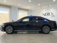 The black Audi A8 L VR10 Armoured car is shown in side profile with blue emergency lights, inside a showroom in Madrid.