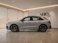 The 2022 Audi RS Q8 in metallic silver, viewed from its side profile, is displayed in a modern showroom in Lausanne.