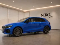 The Gloss Blue 2023 Audi RS3 Performance Edition is showcased from a front three-quarter view in a modern showroom in Zurich.