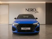 The gloss blue Audi RS3 Performance Edition is shown from a head-on front view inside a modern showroom in Zurich.
