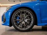 The front wheel of the blue 2023 Audi RS3 Performance Edition, showcasing its intricate rim and blue brake caliper, in Zurich.