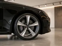 Close-up of the gloss black Audi RS4's front wheel, showcasing its silver multi-spoke rim and brake caliper in Zurich.