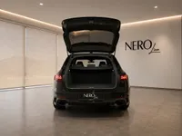 The gloss black 2024 Audi RS4 Avant is seen from the rear with its trunk open, parked indoors in Zurich.