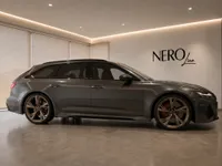 The 2023 Audi RS6 Avant Performance in gloss dark metallic grey is parked sideways in a luxury showroom in Lausanne.