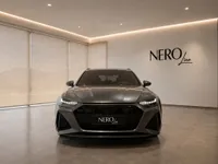 The gloss dark metallic grey 2023 Audi RS6 Avant Performance is showcased from the front in a luxury showroom in Lausanne.