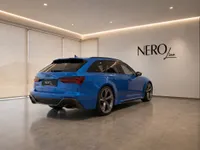 The blue 2023 Audi RS6 Avant Performance is showcased from a rear three-quarter angle in a modern showroom in Zurich.