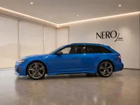 The bright blue 2023 Audi RS6 Avant Performance is shown in side profile within a modern showroom in Zurich.