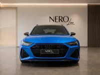 The bright blue Audi RS6 Avant Performance is prominently displayed from the front in a modern NEROline showroom in Zurich.