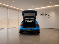 The blue Audi RS6 Avant Performance is shown from the rear with its trunk open in a showroom in Zurich.