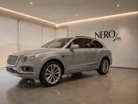 A sleek Gloss Silver Bentley Bentayga V8 is elegantly displayed in a modern showroom in Lausanne, featuring the NEROline logo.