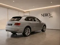The Gloss Silver Bentley Bentayga V8 is parked in a modern showroom, captured from a rear three-quarter angle in Lausanne.
