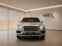 Front view of the luxurious Gloss Silver Bentley Bentayga V8 SUV with headlights on, displayed in a modern showroom in Lausanne.