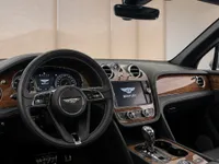 The luxurious interior of the Bentley Bentayga V8 in Lausanne, featuring the steering wheel, infotainment screen, and elegant wood trim.