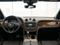 The luxurious interior cockpit of the Bentley Bentayga V8 in Lausanne, featuring a steering wheel, dashboard, and infotainment screen with wood trim.