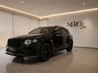 A gloss black 2021 Bentley Bentayga V8 is elegantly displayed in a modern showroom in Zurich, showing its front and side.
