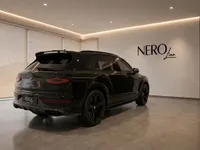 A sleek black Bentley Bentayga V8 is parked in a modern showroom in Zurich, viewed from its rear three-quarter angle.